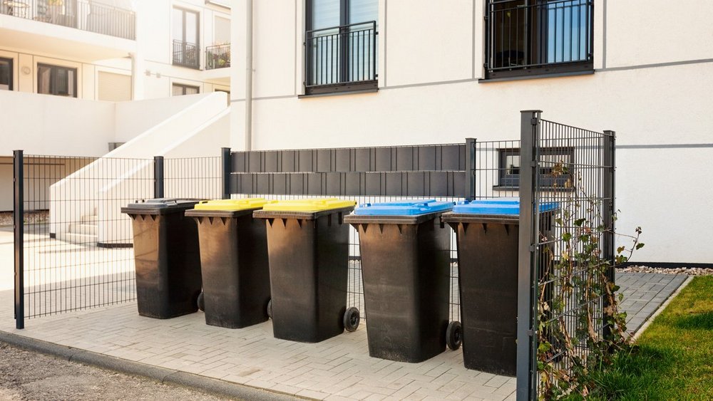 A row of rubbish bins stand neatly in front of a new building