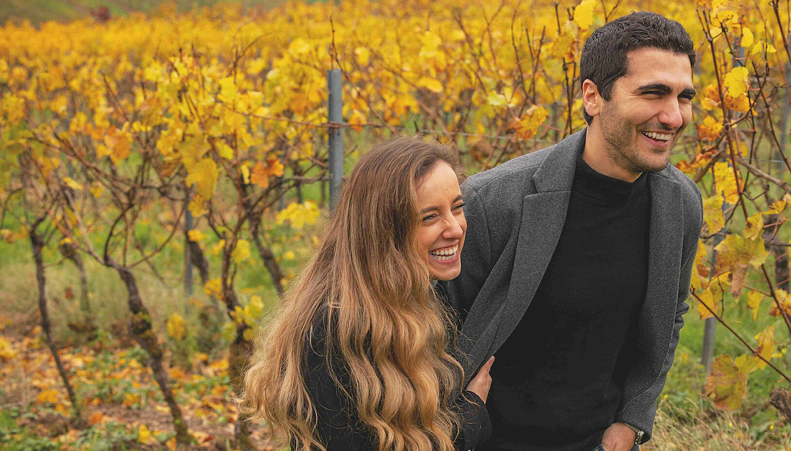 Two people standing in a vineyard talking to each other in sunshine.